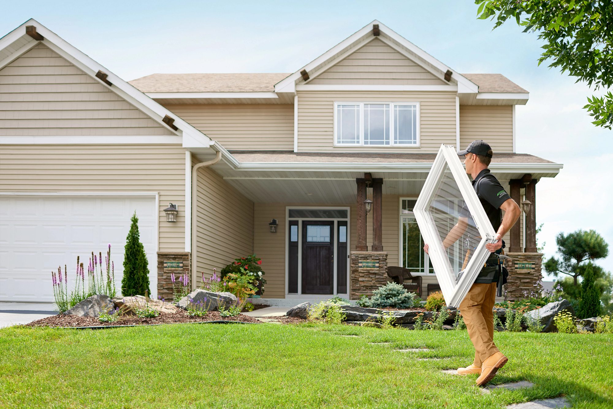 man in work uniform carrying window into home